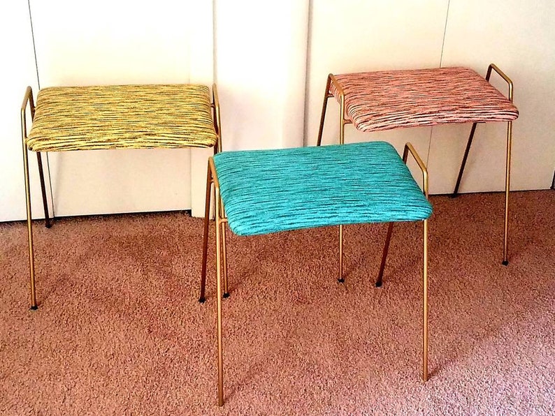 May include: Three gold metal framed stools with different colored patterned fabric upholstery. The stools are on a light brown carpet.