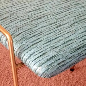 May include: A close-up of a teal blue upholstered bench with a gold metal frame. The bench has a striped pattern and is sitting on a red carpet.