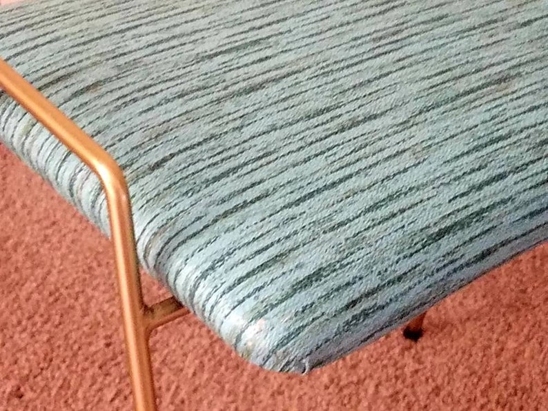 May include: A close-up of a teal blue upholstered bench with a gold metal frame. The bench has a striped pattern and is sitting on a red carpet.