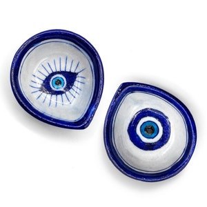 Puede incluir: Dos cuencos pequeños de cerámica blanca con bordes azules y un diseño de ojo turco azul. Los ojos turcos están pintados en tonos de azul y blanco.