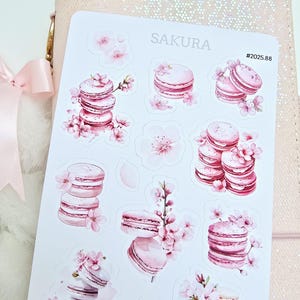 May include: A sheet of pink and white stickers featuring macarons and cherry blossoms. The stickers are labeled "Sakura" and "#2025.88".