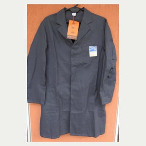 Puede incluir: Una bata de laboratorio gris oscuro con cuello de solapa, mangas largas y tres bolsillos. La bata tiene una etiqueta con la marca "SAHLBERG" y un pequeño parche en el pecho. La bata está colgada en una percha negra.