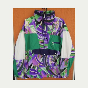May include: A colorful, multi-patterned jacket with a zipper closure and a snap button flap pocket. The jacket features a green, purple, and white color scheme with a variety of geometric and star-shaped designs. The text "Speed" is repeated throughout the design.