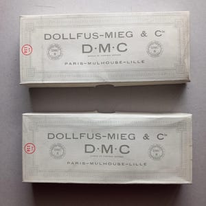 Puede incluir: Dos cajas rectangulares con el texto "DOLLFUS-MIEG & Cie D.M.C PARIS-MULHOUSE-LILLE" en gris claro. Las cajas tienen un borde decorativo y un logotipo circular. El número "116" es visible en el lado izquierdo.