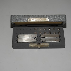 Peut inclure: Un coffret de rangement en métal gris contenant un jeu de jauges de filetage de précision et de petites goupilles métalliques. Le coffret possède un couvercle à charnière avec un loquet. Les jauges portent des gravures 55° et 60°.