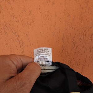 May include: A black cap featuring a white interior fabric label with the printed text: Zeppelin Rental GmbH & Co. KG, Graf-Zeppelin-Platz 1, D-85748 Garching b. M&uuml;nchen, (Lot-Nr.: 39996). The label is attached to the inner lining of the headwear.