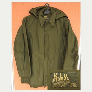 May include: An olive green hooded jacket with a button-up front and a drawstring waist. The jacket has a label with text. The jacket is hanging on a black hanger.