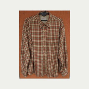 May include: A long-sleeve button-down shirt featuring a plaid pattern in shades of rust orange, tan, and muted green. The shirt includes a pointed collar, a single chest pocket on the left side, and a full-length front button closure with light buttons.