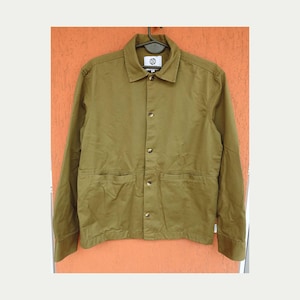 May include: Olive green jacket with a button-up front, two front pockets, and a collar. The jacket is hanging on a black hanger. The jacket has a small white tag on the sleeve. The jacket is made of a durable fabric.