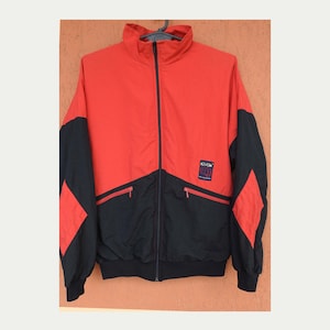 May include: A red and black windbreaker jacket with a zip fastening and a logo patch that says "K-WAY" on the left chest.