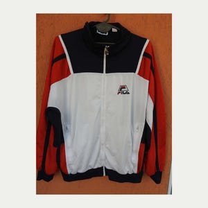 Puede incluir: Una chaqueta deportiva de manga larga con un dise&ntilde;o de bloques de color en azul marino, blanco y rojo. La chaqueta tiene cuello alto, cremallera frontal completa y dos bolsillos laterales con cremallera. El logotipo de Fila est&aacute; bordado en el pecho.