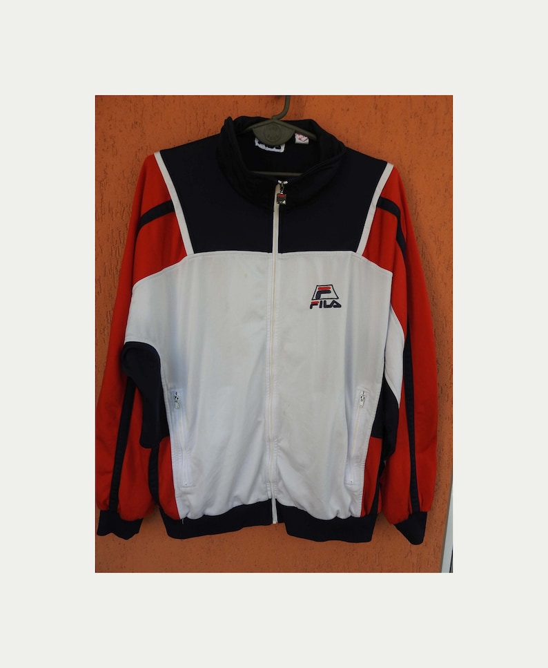 Puede incluir: Una chaqueta deportiva de manga larga con un dise&ntilde;o de bloques de color en azul marino, blanco y rojo. La chaqueta tiene cuello alto, cremallera frontal completa y dos bolsillos laterales con cremallera. El logotipo de Fila est&aacute; bordado en el pecho.