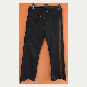 May include: Black pants featuring a vertical brown stripe running down the outer side of the left leg. The pants include a front button and zipper closure, belt loops, and two front pockets, all displayed on a black plastic clothing hanger.