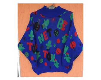 May include: A blue knitted jumper with a colourful pattern of planets, stars, and the words "To Wet To Town" and "Be".