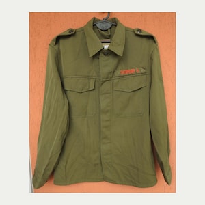 Puede incluir: Una camisa verde de estilo militar con un parche bordado en rojo que dice "TIEFENBRUNNER".