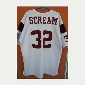 Pode incluir: Camisola branca com detalhes bordô, com a palavra "SCREAM" nos ombros e o número "32" nas costas. A camisola tem listras bordô nas mangas.