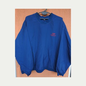 May include: A solid blue long-sleeve pullover windbreaker jacket with a crew neckline and elastic cuffs. The chest features the red embroidered text CGP Continental Gas & Plastic Inc. The garment is displayed on a black plastic hanger.