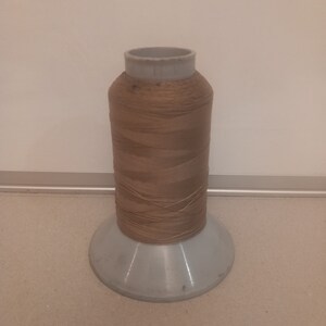 May include: A spool of brown thread on a white plastic bobbin.
