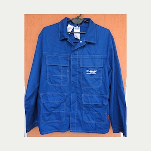 May include: A royal blue work jacket featuring a classic collar, long sleeves, and a button-up front. The garment includes four front pockets with flaps and displays the white BASF logo and the text We create chemistry on the upper right pocket.
