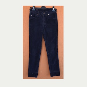 Puede incluir: Pantalones de pana azul marino oscuro colgados de una percha negra. Los pantalones tienen cintura alta, bolsillos y pernera recta. La tela de pana tiene un sutil acanalado vertical. Estilo clásico.