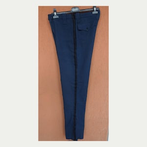 Pode incluir: Calças azul marinho com uma faixa preta na lateral, penduradas em um cabide preto. As calças têm um bolso nas costas e são feitas de um tecido liso. O fundo é uma parede texturizada, laranja-marrom.