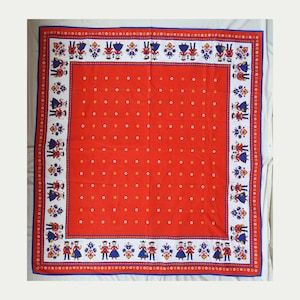 Può includere: Tessuto quadrato rosso con bordo bianco e rifiniture blu. Il bordo presenta figure in abiti tradizionali. Il centro è rosso con piccoli motivi floreali bianchi e gialli. Questo tessuto potrebbe essere una sciarpa o una tovaglia.