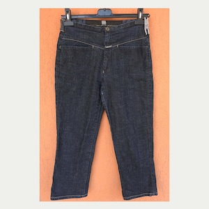 Puede incluir: Pantalones capri vaqueros de color azul oscuro colgados de una percha negra. Los capris tienen una cintura alta, cierre de botón y un diseño de costura único en la parte delantera. Los pantalones miden unos 76 cm de largo.