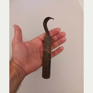 Peut inclure: Un outil à main doté d'un manche cylindrique en bois brun foncé et d'une lame métallique incurvée et pointue. La partie métallique est fixée au sommet du manche et s'étend vers le haut avec une forme de crochet distincte. Le bois est usé.