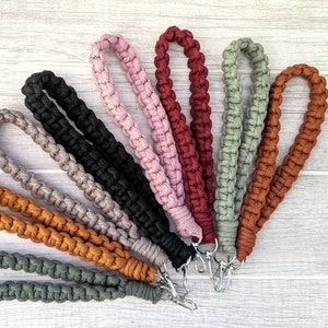 May include: A collection of nine braided cord keychains in various colors, including black, gray, brown, pink, red, and green. Each keychain has a silver metal clasp.