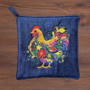 May include: A square dark blue denim potholder featuring a vibrant embroidered rooster design. The rooster is composed of colorful floral and swirling patterns in shades of red, yellow, orange, green, and blue, with a small fabric loop at the corner.