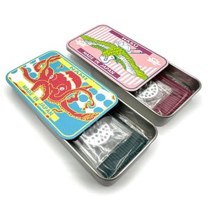 May include: Two rectangular metal tins containing incense sticks and a small metal holder. The left tin features a red octopus graphic with the text NAMI and MADE IN JAPAN. The right tin shows a green crane graphic with the text HASU and MADE IN JAPAN.