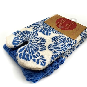May include: White and blue split-toe socks with a floral design, placed on a blue knitted base. A brown tag with Japanese text is attached. These socks are designed for comfort and style, a traditional Japanese design.