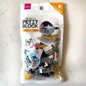 May include: A clear plastic bag containing a Petit Block Java Sparrow building set. The set includes 72 pieces and is recommended for ages 12+. The assembled bird is grey, black, pink, and gold.