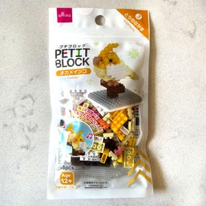 May include: A packet of Petit Block construction bricks, featuring a yellow and white cockatiel model. The package contains 108 pieces and is suitable for ages 12+. The packaging includes Japanese text and an image of the completed bird.