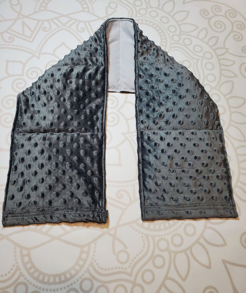 May include: Gray weighted neck wrap with a soft, textured fabric. The wrap has multiple pockets filled with weighted beads.