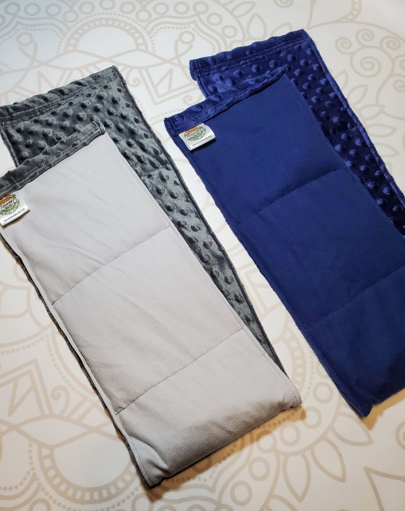 May include: Two weighted blankets, one gray and one navy blue, with a white inner layer and a textured outer layer. Both blankets have a small green and orange label with the text "Weighted Wonders".