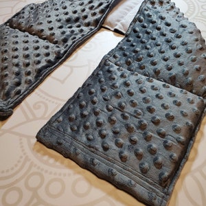 May include: Gray weighted neck wrap with a textured fabric and a soft, plush feel. The wrap is designed to provide comfort and relaxation.