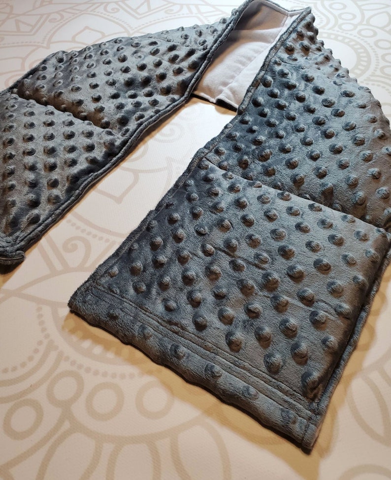 May include: Gray weighted neck wrap with a textured fabric and a soft, plush feel. The wrap is designed to provide comfort and relaxation.