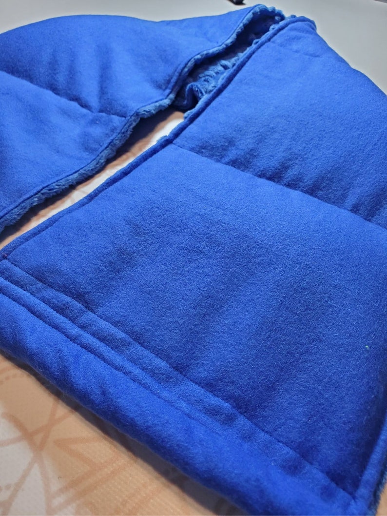May include: A blue fleece neck wrap with a soft, plush lining. The wrap is quilted with multiple compartments for added warmth and comfort.