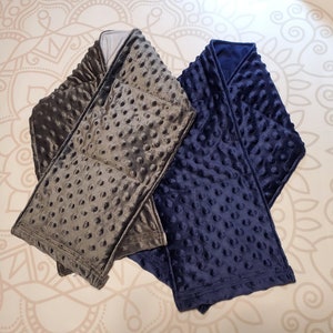 May include: Two weighted blankets, one gray and one navy blue, with a textured, quilted design. The blankets are folded and arranged on a patterned surface.