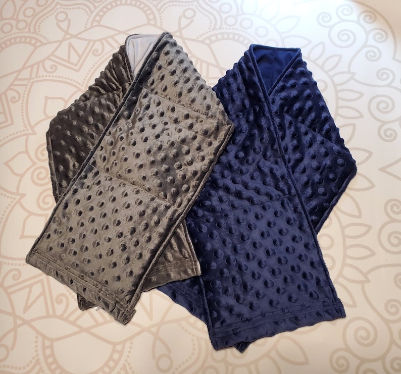 May include: Two weighted blankets, one gray and one navy blue, with a textured, quilted design. The blankets are folded and arranged on a patterned surface.