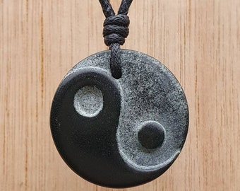 May include: A black and white yin yang pendant necklace with a black cord. The pendant is made of smooth, polished stone.