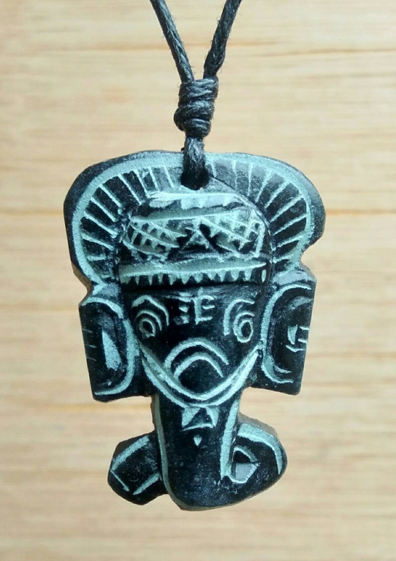 May include: A black and green carved wooden pendant of an elephant head with a black cord necklace.