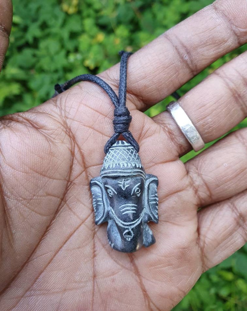 Pode incluir: Um pingente de pedra talhada em preto e cinza da divindade hindu Ganesha, em um cord&atilde;o preto.