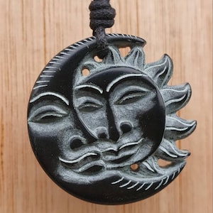 May include: Black and white carved wooden pendant of a sun and moon with faces. The pendant is on a black cord.