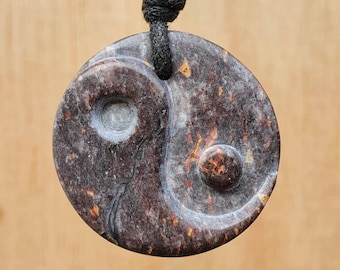 May include: A black cord necklace with a brown and black yin yang pendant. The pendant is made of stone and has a speckled pattern.