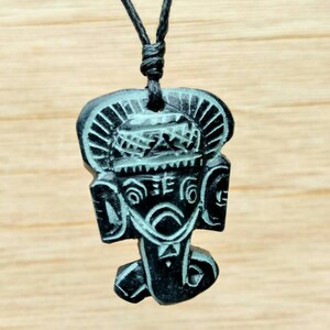 May include: Black necklace with a carved wooden pendant featuring a stylised face with intricate details.