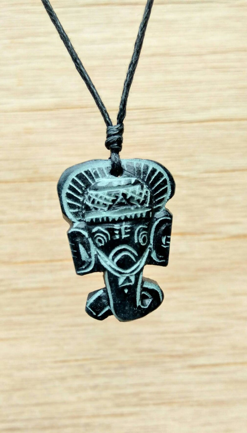May include: Black necklace with a carved wooden pendant featuring a stylised face with intricate details.