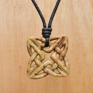 Op de afbeelding: Een vierkante hangerketting met een Keltisch knoopontwerp, gesneden uit lichtbruin hout. De hanger hangt aan een zwart koord.