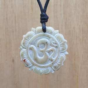 May include: A white stone pendant with a carved Om symbol inside a flower design, hanging from a black cord.